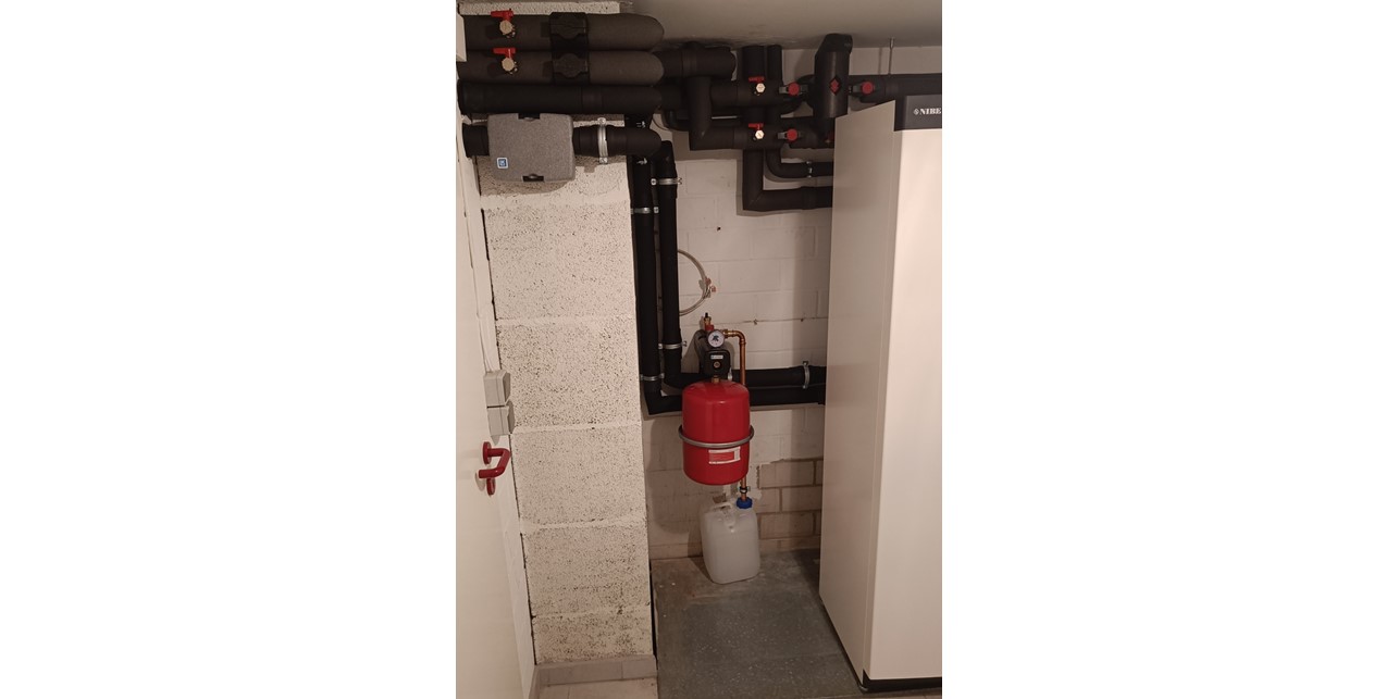Links neben der Erdwärmepumpe sind weitere Anschlussleitungen und ein Ausdehnungsgefäß montiert.