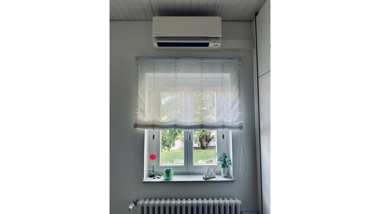 Ein Split-Klimagerät über und ein Guss-Heizkörper unter einem Fenster.
