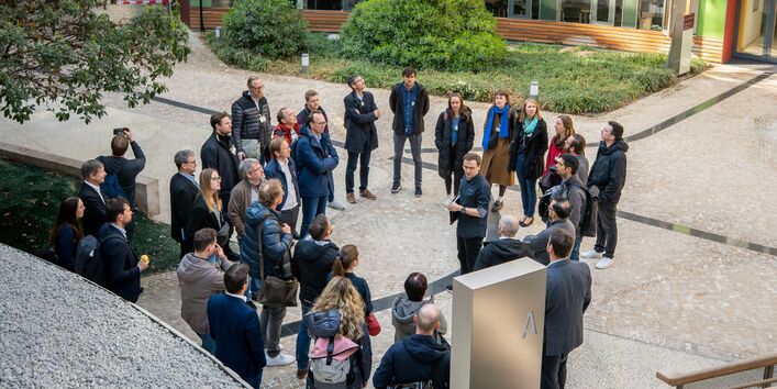 Eine Gruppe von etwa 25 Menschen steht kreisförmig im Atrium des UBA-Gebäudes und verfolgt die Ausführungen eines Guides.