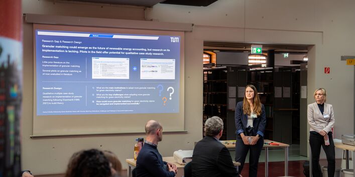 Eine Person referiert stehend, während weitere Personen sitzend den Workshop verfolgen. Im Hintergrund wird eine Präsentation projiziert.