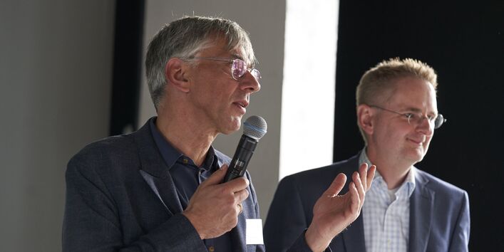 Das Foto zeigt Stefan Tidow (BMUV) mit Mikrofon und Martin Schmied (UBA) bei der Begrüßung der Teilnehmenden.