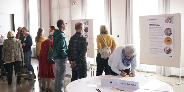 Mehrere Menschen stehen vor Schautafeln, die die Folgen der Klimakrise für die Gesundheit aufzeigen.
