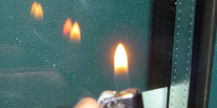 Feuerzeugtest: Jemand hält ein Feuerzeug vor die Verglasung und es spiegelt sich die Flamme an der Glasoberfläche. 