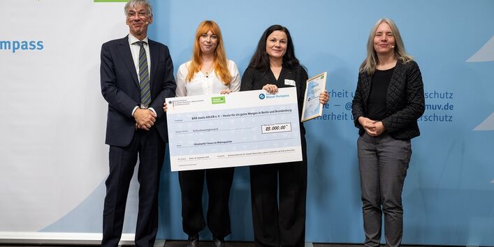 Stefan Tidow und Dr. Bettina Rechenberg überreichen einen Scheck an die Gewinnerinnen des Vereins "BÄR meets ADLER e.V. - Verein für ein gutes Morgen in Berlin und Brandenburg".