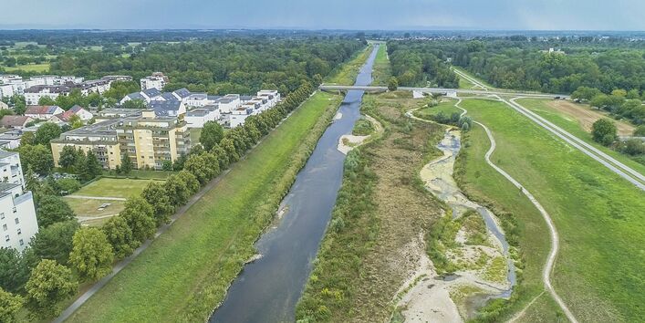 Luftbild der renaturierten Murg. Im Vordergrund liegt ein geschwungenes Nebengewässer mit Kiesbänken, Laufweitungen und Verengungen. Im Hintergrund liegt der reaktivierte Auwald.