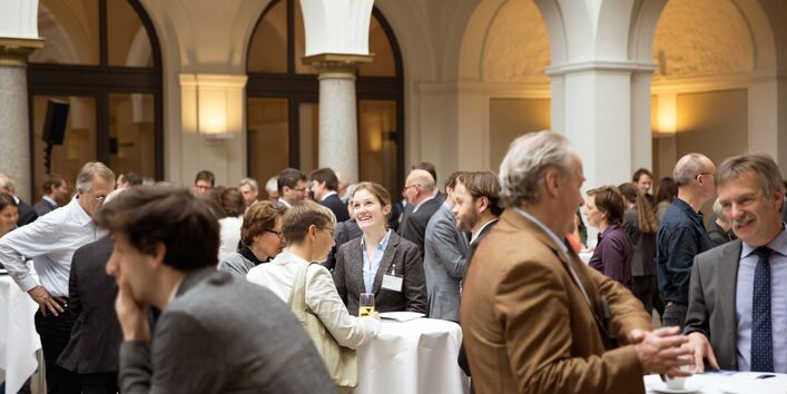 Teilnehmende stehen in einer Pause an Stehtischen und unterhalten sich