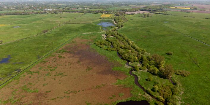 Luftbild des Entwicklungskorridors der Wümme mit Sträuchern und Bäumen im Uferbereich, der sich deutlich vom benachbarten Grünland und Acker abgrenzt und weit durch die Landschaft zieht.
