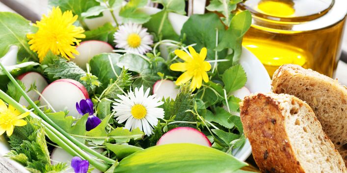 Dekorativer Wildkräutersalat mit zwei Scheiben Brot und einer Flasche Öl auf einem Tisch