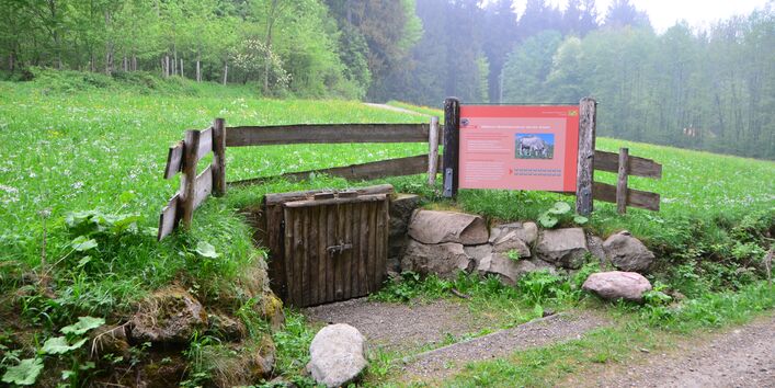 Ein Bodenprofil hinter einem Holztor und eine Tafel daneben