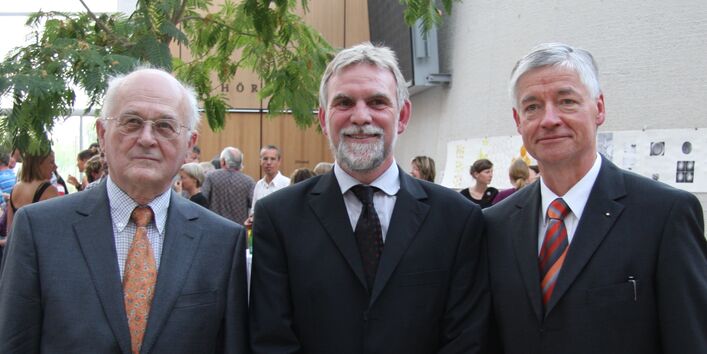 drei Männer im Anzug stehen in einer Reihe aufgestellt im UBA-Gebäude Dessau und schauen in die Kamera