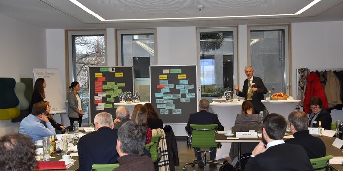 Burkhard Huckestein spricht vor Teihnehmenden der Veranstaltung, auf einer Flipchart Zettel mit Stichworten