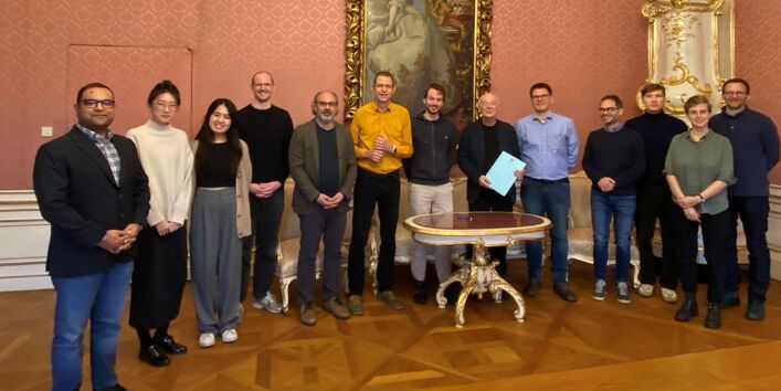 12 participants of the workshop stand together with IIASA Director General John Schellnhuber in a baroque furnished room at IIASA.