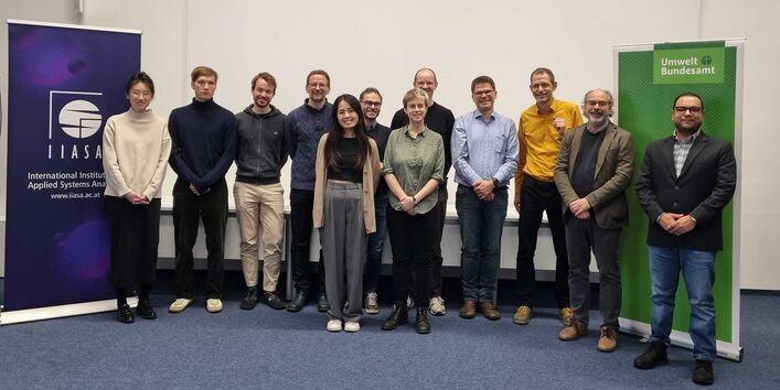 The 12 participants stand next to each other in a meeting room at IIASA.