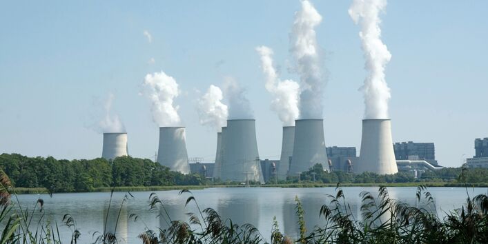 dampfende Kühltürme eines Kraftwerks an einem Gewässer