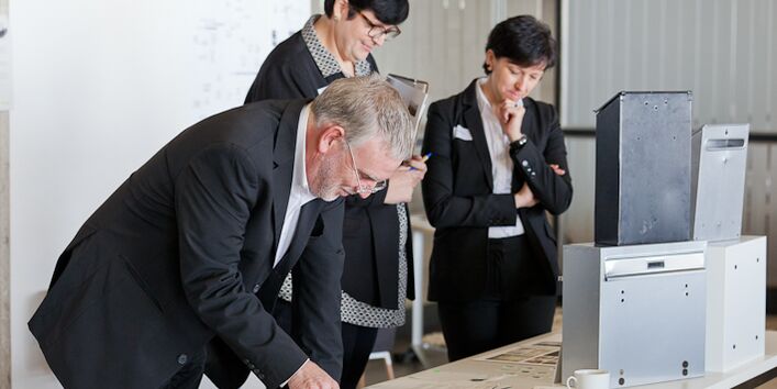 ein Mann und zwei Frauen schauen sich auf einem Tisch liegende Gegenstände und Ausdrucke an.