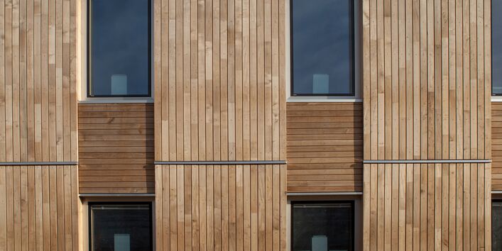 Fassade mit Holztafeln verkleidet, die Holztafeln bilden ein Raster aus größeren senkrechten Tafeln mit senkrechten Holzlatten und kleineren waagerechten Tafeln mit waagerechten Holzlatten