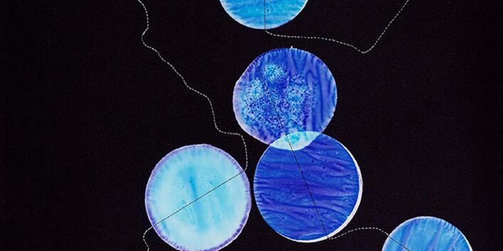 runde, blaugefärbte Stoffstücke mit einem Faden verbunden vor schwarzem Hintergrund