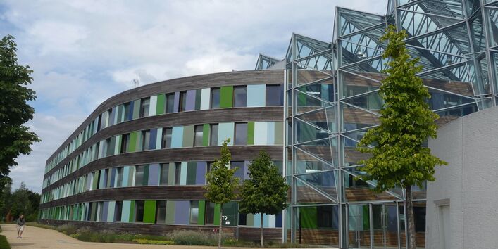 Main entrance of UBA office building in Dessau-Roßlau with glass façade. The remaining façade is made of wood, windows, and glass slabs in shades of green and blue
