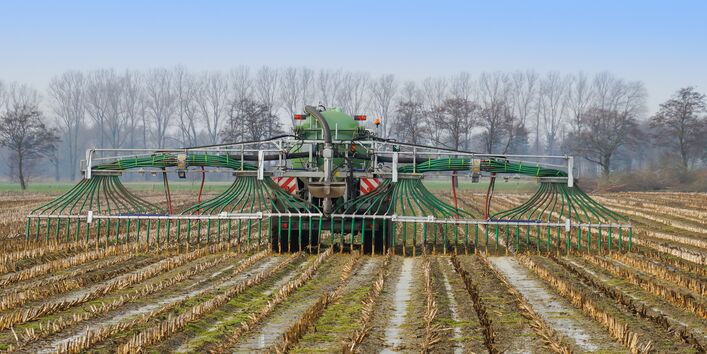Ein Traktor bringt Gülle mit Schleppschläuchen auf einem abgeernteten Feld aus