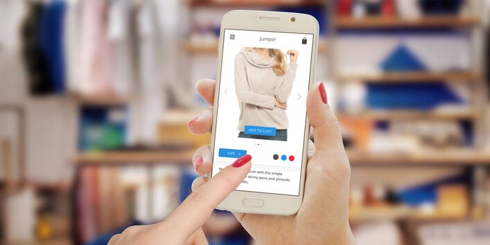 A woman orders clothing online, sitting in front of her wardrobe.