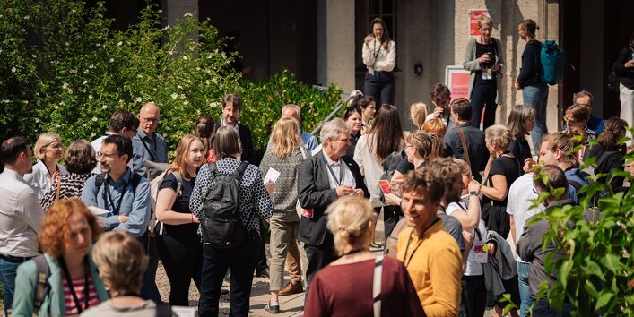 Teilnehmerinnen und Teilnehmer der Konferenz 'Gemeinsam. Neues Europäisches Bauhaus Weiterdenken' stehen im Innenhof, unterhalten sich und halten Programmhefte in der Hand.