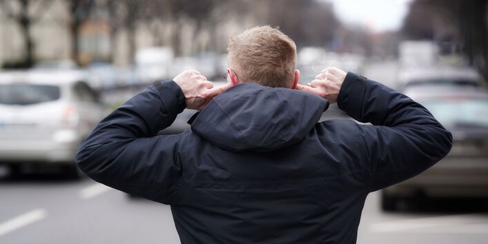 A man covers his ears on a busy city street