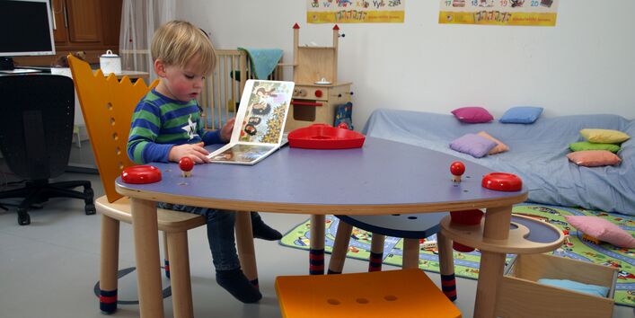 Kind sitzt an einem fisch und blättert in einem Bilderbuch.