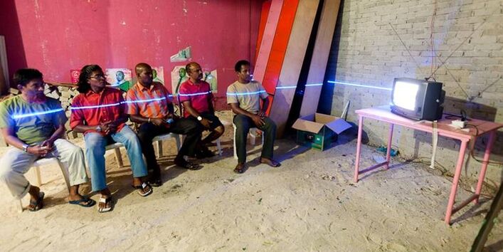 Eine Gruppe von Männern die fernsehn guckt. Das Kunstprojekt zeigt, dass bei gestiegenem Wasserpegel bis zur Brust unter Wasser sitzen würden.