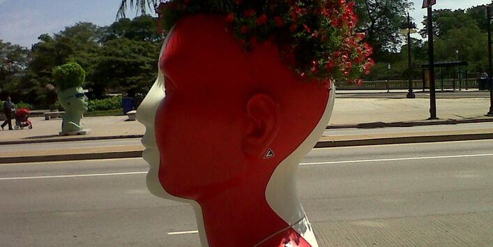 Auf dem Bürgersteig steht ein übergroßer roter Kopf, er dient als Blumentopf.