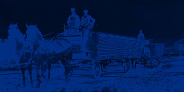 Pfedewagen mit zwei Arbeitern auf dem Kutschbock, die Ladefläche ist mit Metall-Rolläden abgedeckt. 