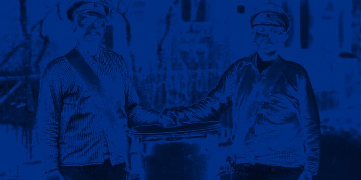 Zwei Männer tragen einen großen Standeimer