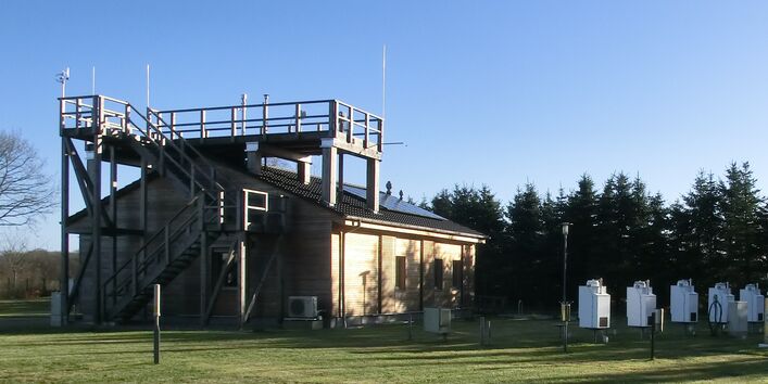 Auf dem Foto sieht man links die UBA-Luftmessstation Zingst und rechts Probenahme-Einrichtungen für die Bestimmung der nassen Deposition von Schwermetallen (Depositionssammler).
