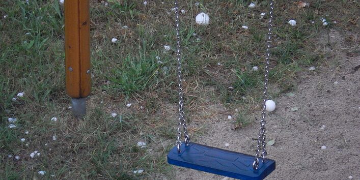 Eine Schaukel blaue Schaukel. Auf dem Boden liegen viele große Hagelkörner.