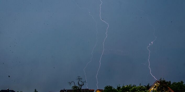 Ein dunkler Himmel mit Blitzen über Häusern.