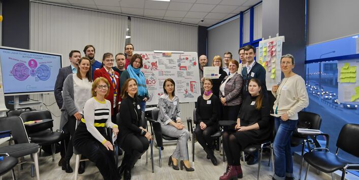 Eine Gruppe von Menschen sitzt bzw. steht vor einem Flipchart.