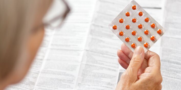 Ältere Frau hält eine Packung mit orangefarbenen Pillen vor einer großen Medikamentenpackungsbeilage