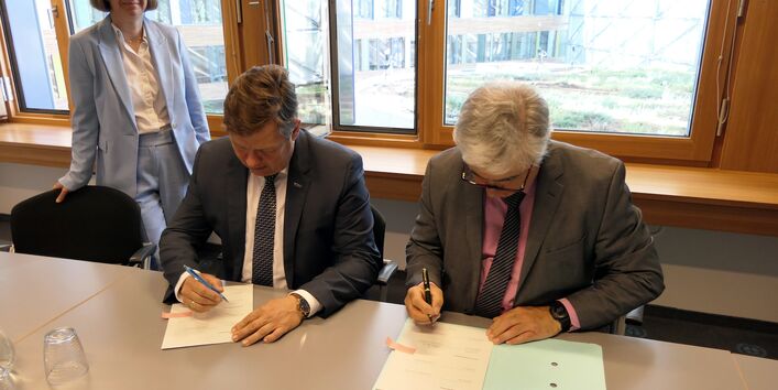 Herr Prof. Dr. Krabbes und Herr Dr. Scheremt unterzeichnen die Vereinbarung am Tisch, Frau Dr. Ranft steht links am Tisch