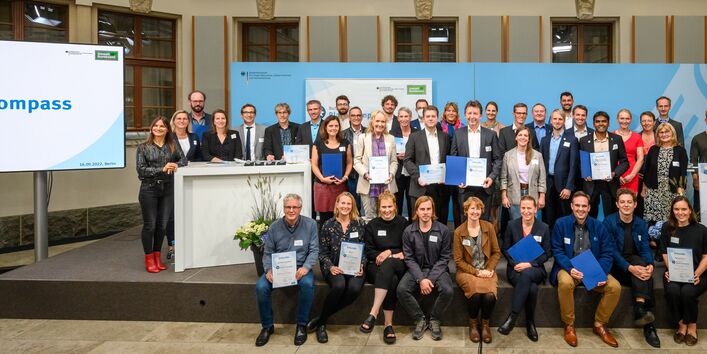 Die Preisträgerprojekte und Nominierten des Bundespreises "Blauer Kompass" 2022 stehen fest und posieren gemeinsam auf der Bühne. Der mit 25.000 Euro dotierte Preis geht jeweils an herausragende Klimanpassungsprojekte in den Bereichen Hochwasserschutz, Landwirtschaft, Handwerk sowie Umweltbildung und ländliche Entwicklung.