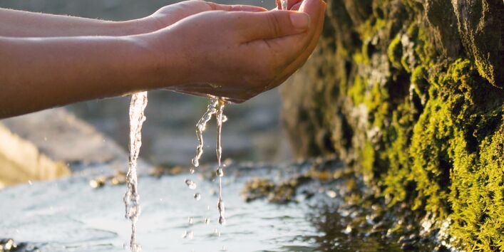 The picture shows two hands catching water emerging from a spring.