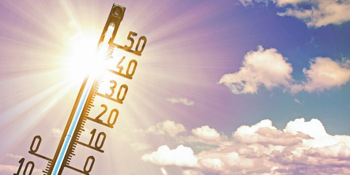 Das Bild zeigt ein klassisches analoges Außentermometer vor einem fast wolkenlosen Himmel mit einer strahlenden Sonne.