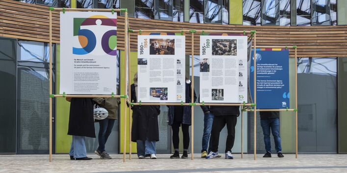 Foto mit den neuen UBA-Ausstellungstalfen in Dessau-Roßlau. Zu sehen ist ein Teil der Ausstellung mit Menschen hinter den Tafeln. 