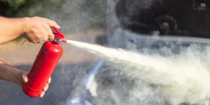 Ein Feuerwehrmann hält den Schlauch, aus dem Schaumlöschmittel quillt, im Hintergrund ist Feuer