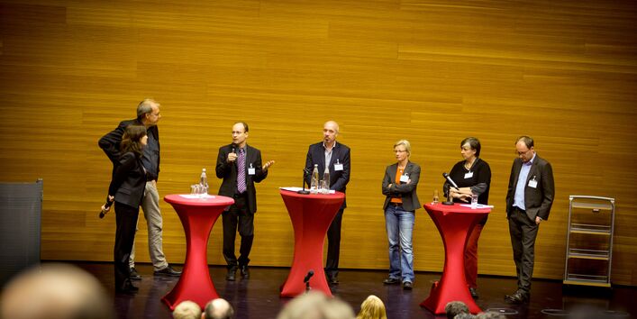 Moderatoren stehen an den Stehtischen auf dem Podium