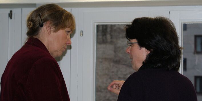 Zwei Teilnehmende stehen vor dem Fenster im Dialog miteinander.