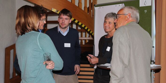 Fünf Teilnehmende sprechen miteinander. Sie stehen dabei vor einer Moderationswand. Im Hintergrund befindet sich eine hölzerne Wendeltreppe.