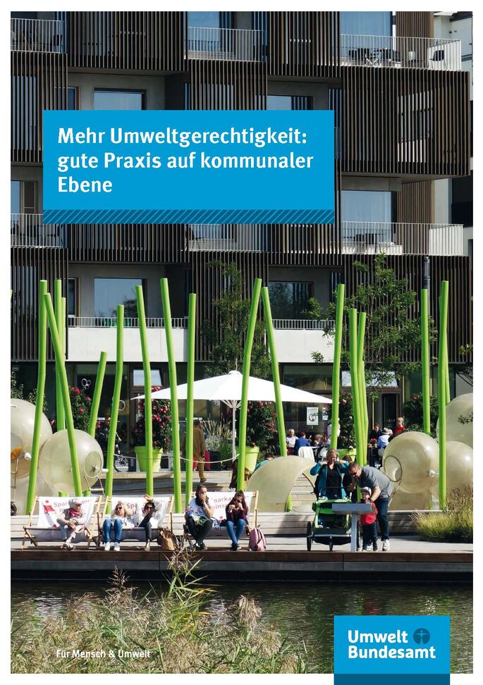 Menschen sitzen an einem Ufer mit Schilf, dahinter ein Gebäude