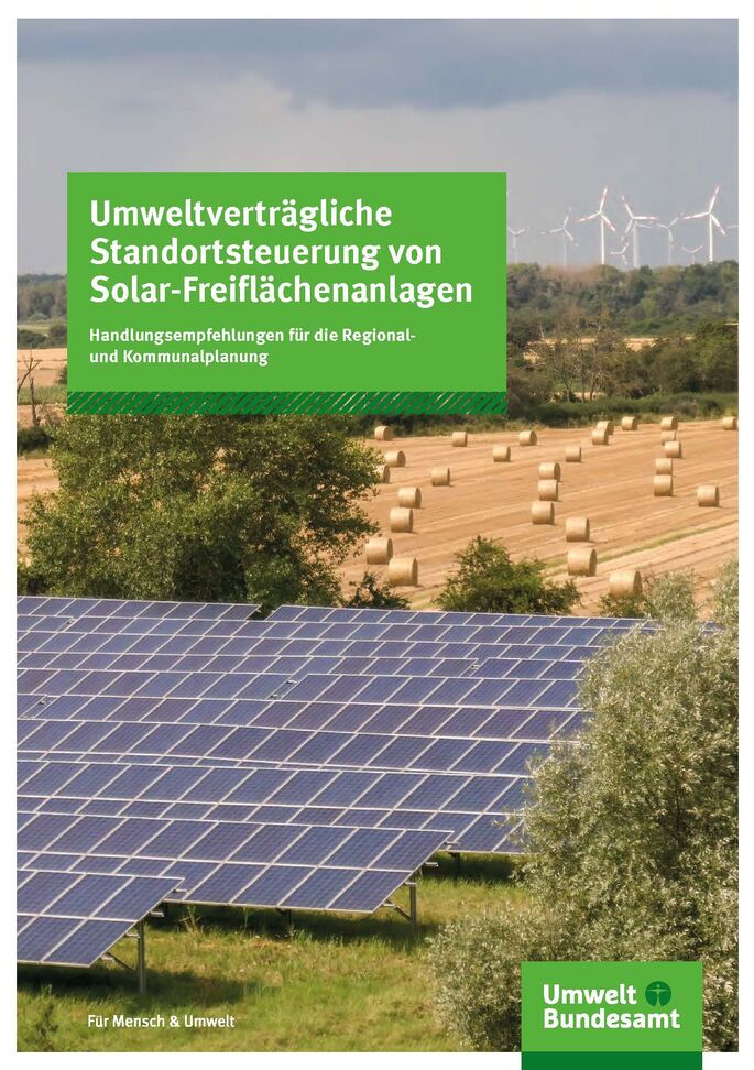 Solaranlagen auf einem Feld, dahinter abgeerntetes Feld und am Horizot Windräder