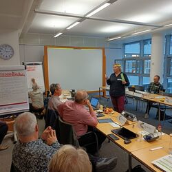 A person in the middle speaks to people sitting at a table during a meeting.