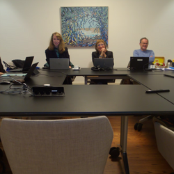 In a small meeting room, 7 people sit at a table.