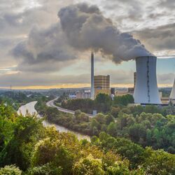 Foto: Zwei Kühltürme eines Wärmekraftwerks im unmittelbaren Umfeld eines Flusses. Aus einem Kühlturm tritt Wasserdampf aus.